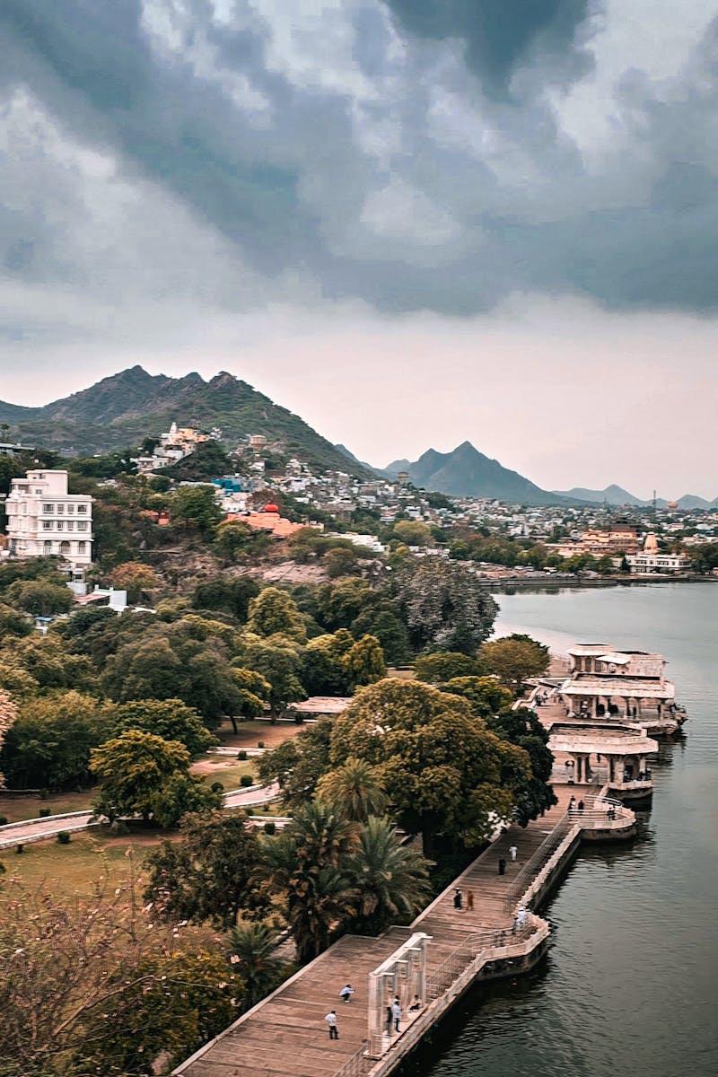 Aerial view of Udaipur's landscape with mountains and lake under dramatic skies.